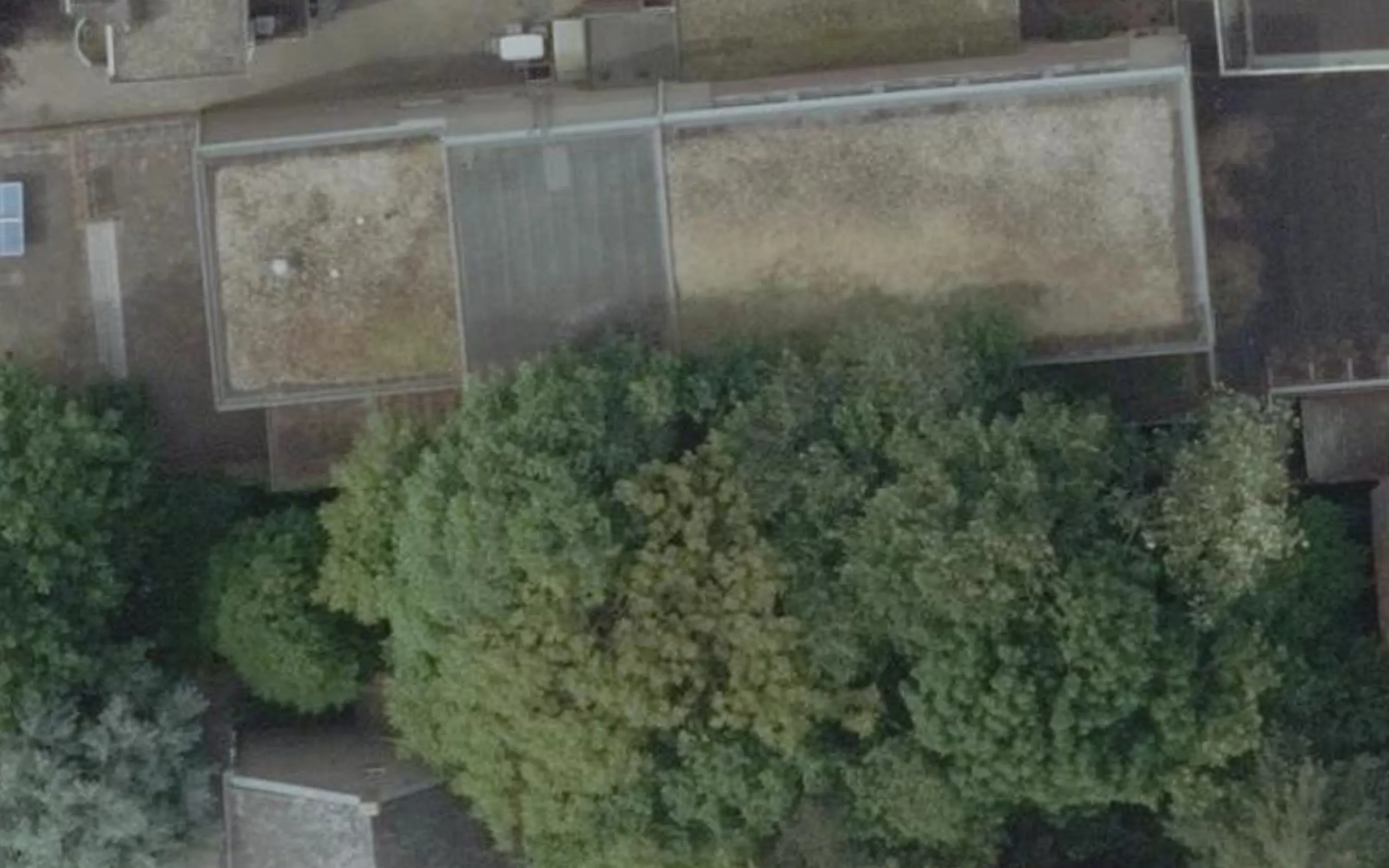 De landelijke luchtfoto uit 2023 van dezelfde plek: het pand en de boomkronen zijn herkenbaar maar onscherp, zonder kaartlagen